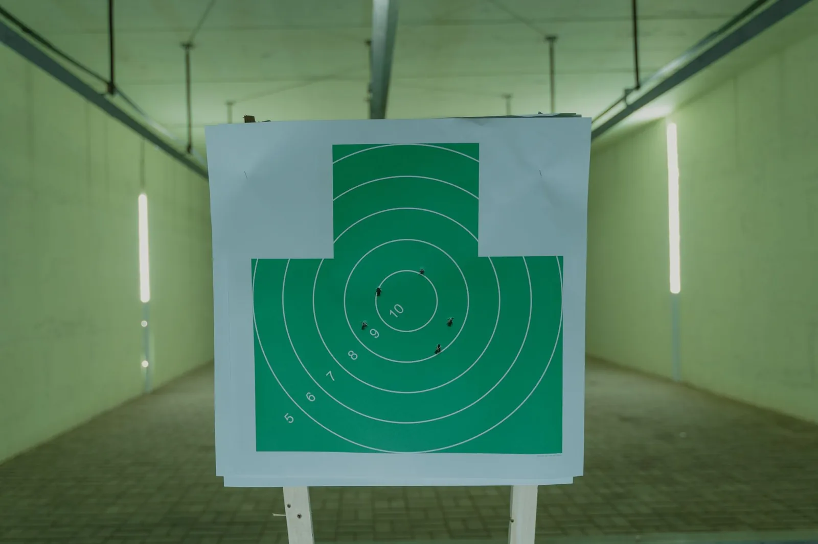 A scored green circle shooting target with bullet holes clustered near the center, mounted on a stand at an indoor range.