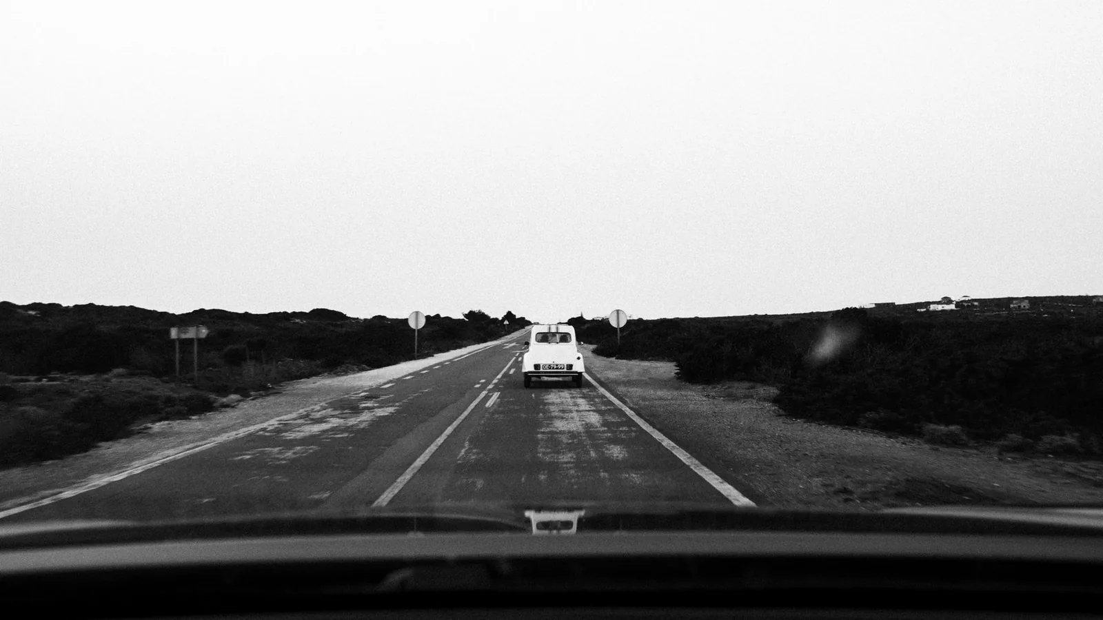 A car ahead on an empty rural highway seen through a windshield