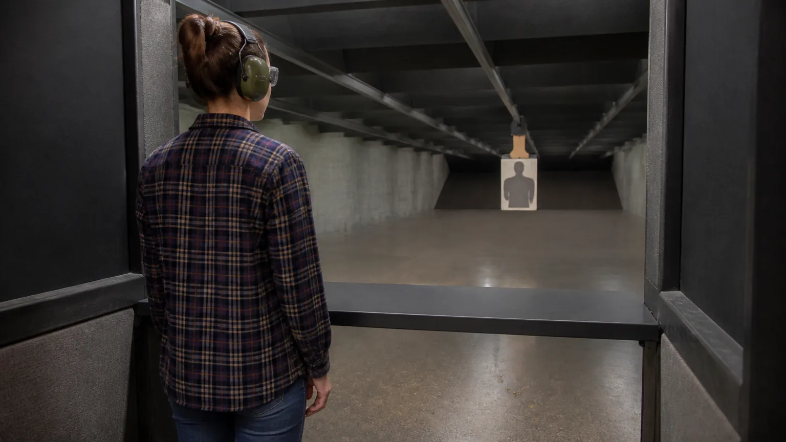 Woman in ear protection at an indoor shooting range lane