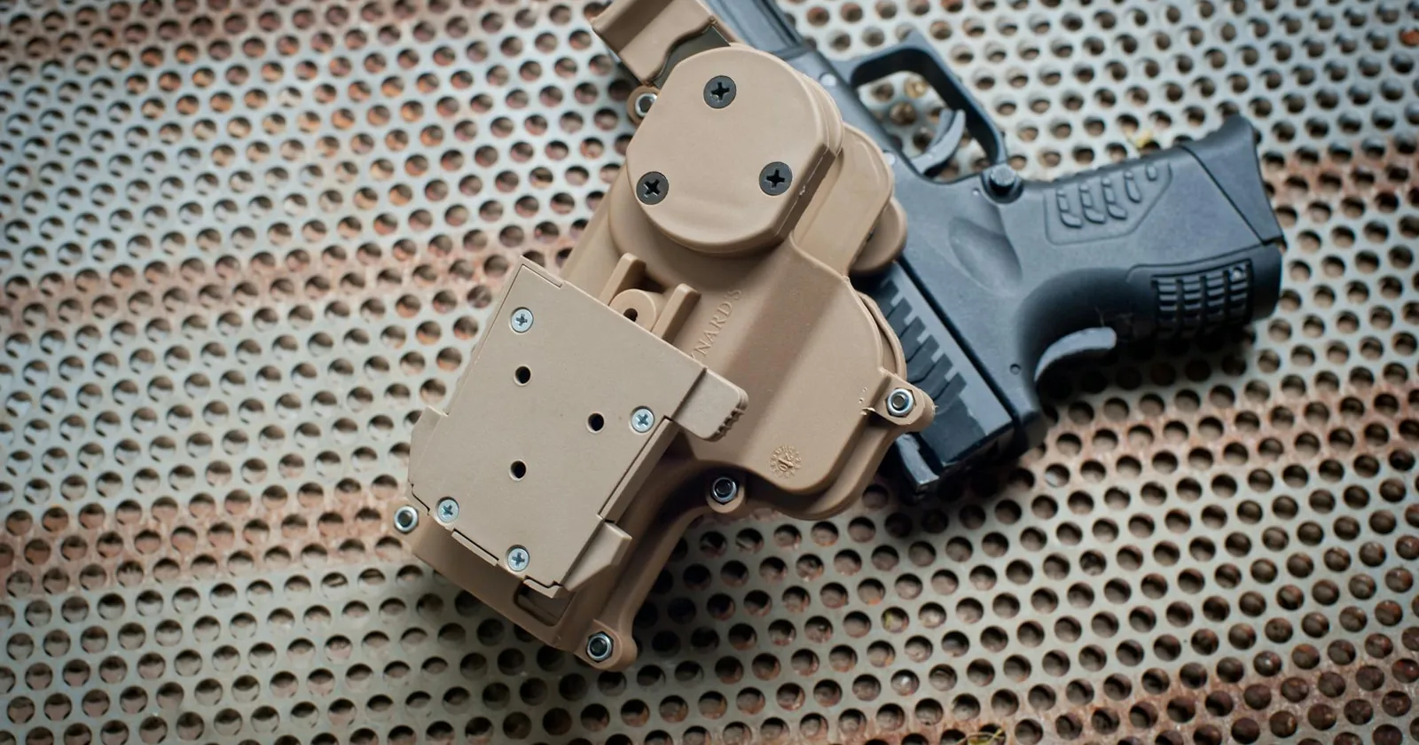 Close-up of a holstered black pistol placed on a perforated metal surface.