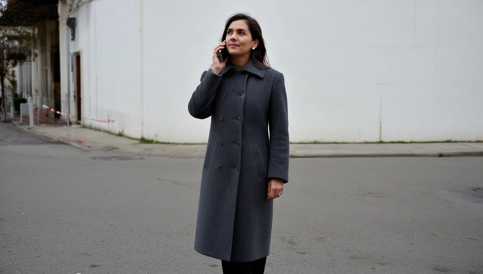 A woman in a long wool coat on a phone call outdoors