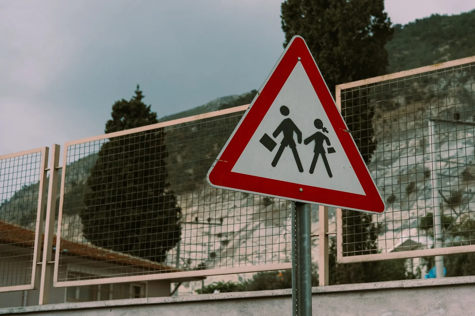 Triangular school crossing warning sign beside a fence