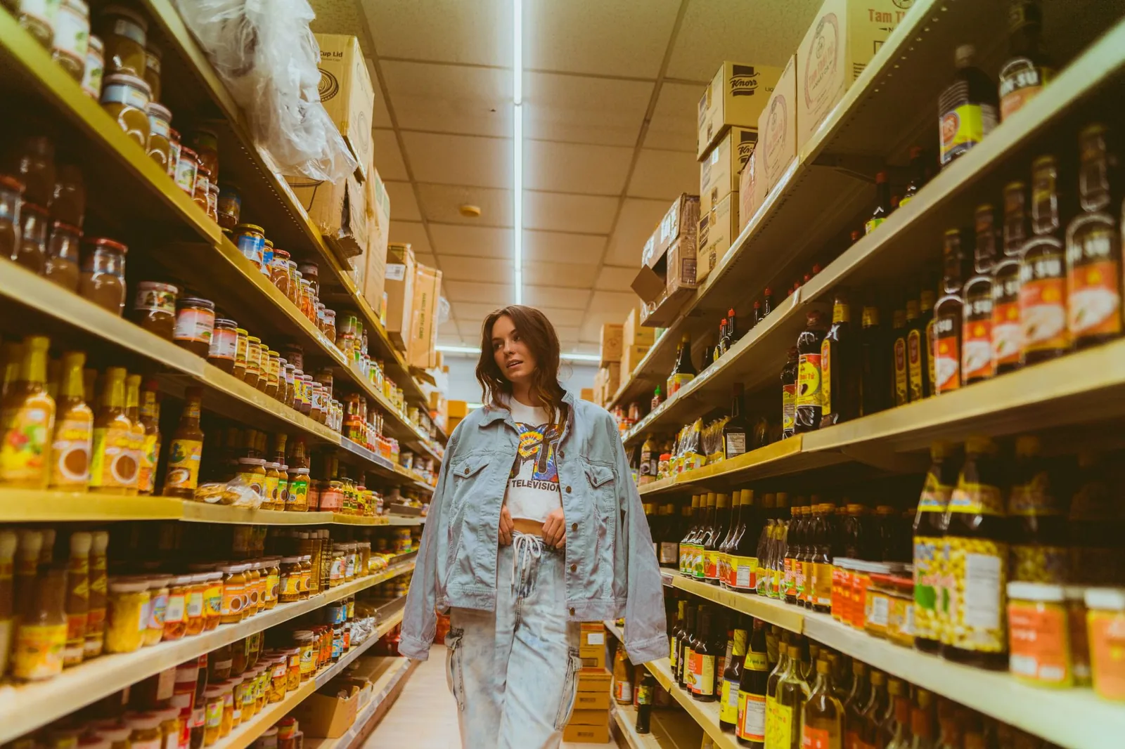 A shopper walking down a grocery store aisle lined with stocked shelves.