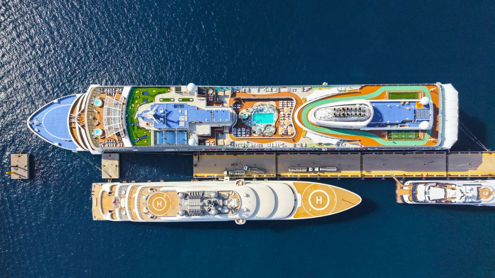 A cruise ship docked at a pier beside a yacht